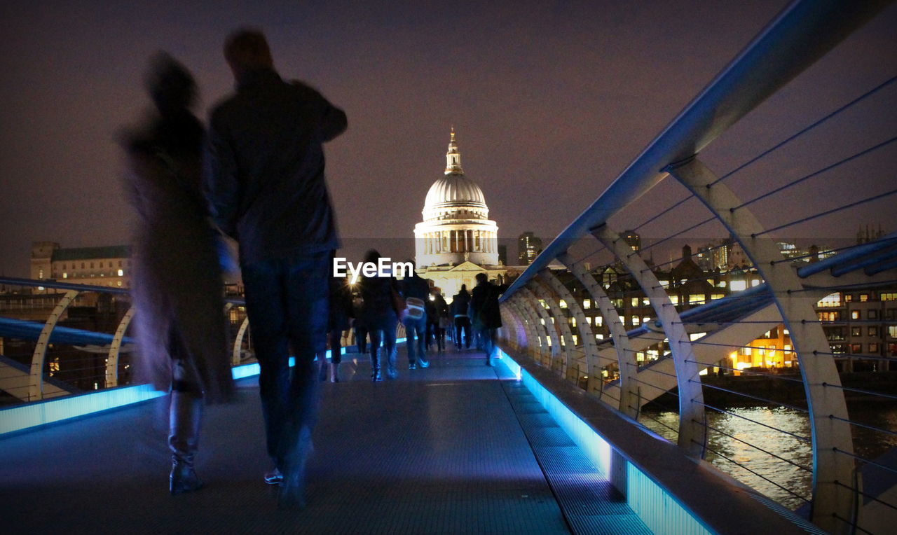 Rear view of people walking on london millennium footbridge at night