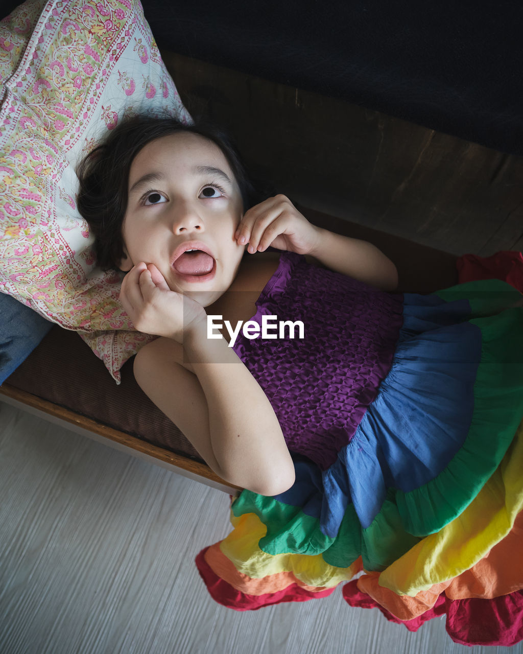 Little girl lying on the long chair with rainbow dress in the living-room. making funny face.