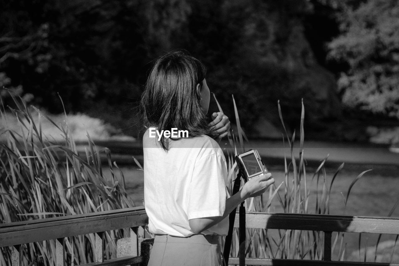 Woman with camera standing against plants