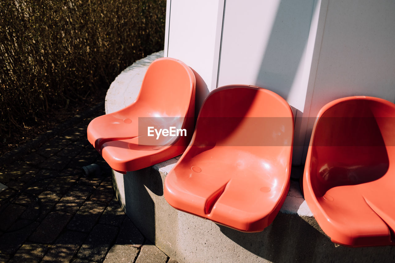 Three red plastic chairs side by side outdoors