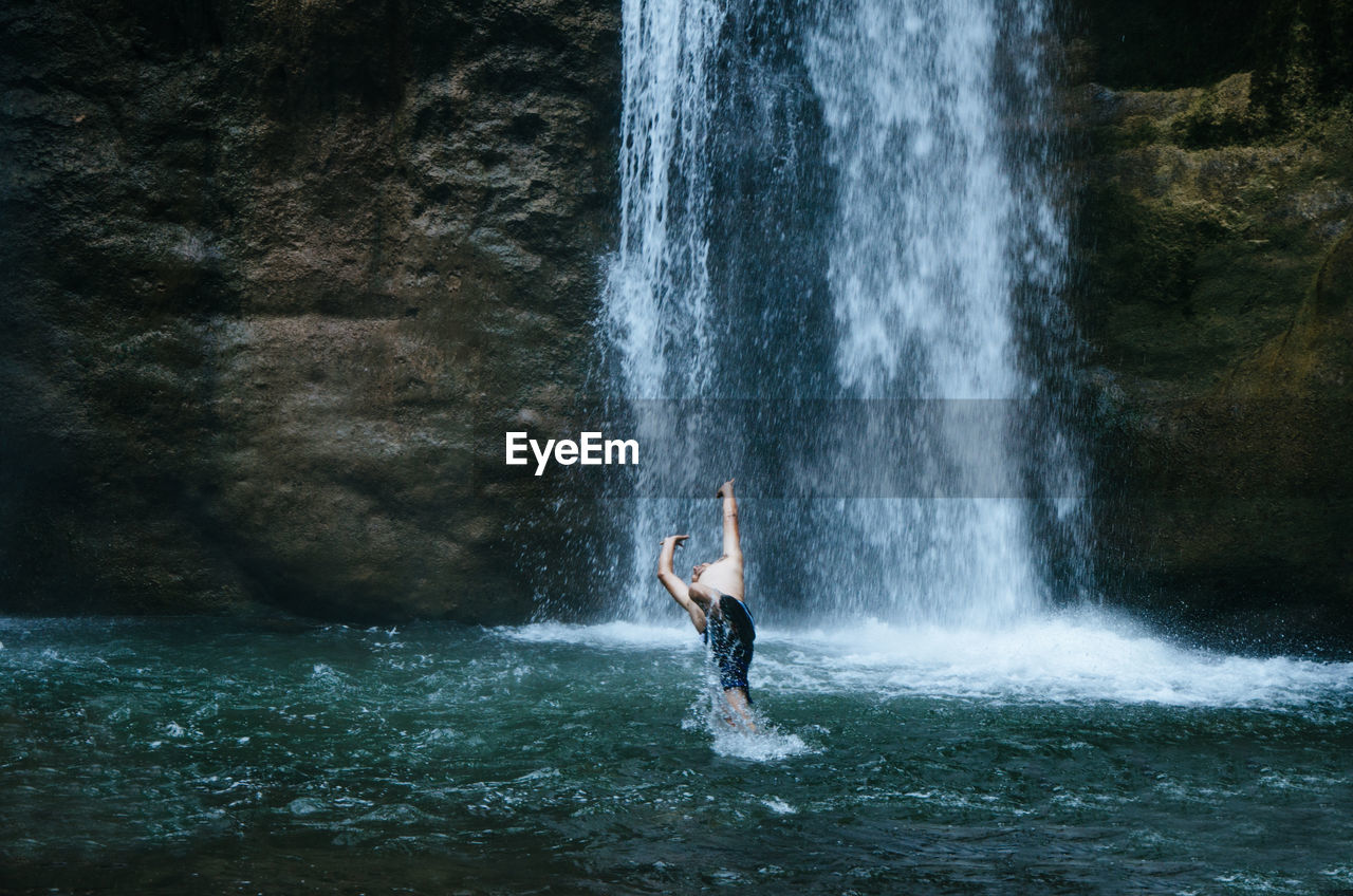 Man splashing water while jumping by waterfall