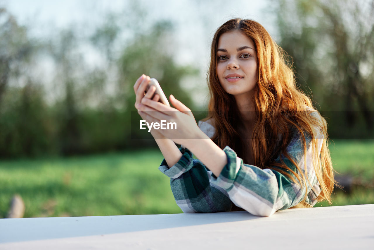 young woman using mobile phone while sitting on field