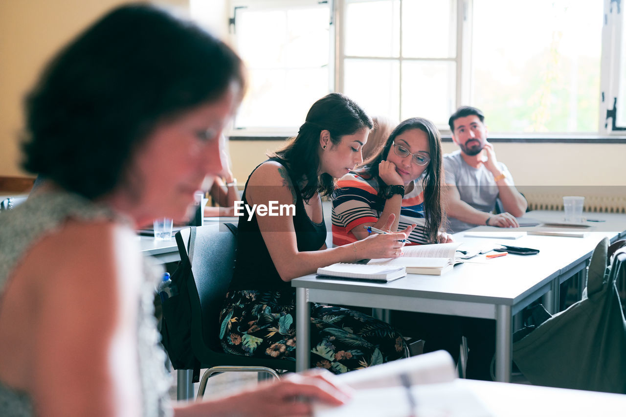 Students discussing over book at desk in classroom