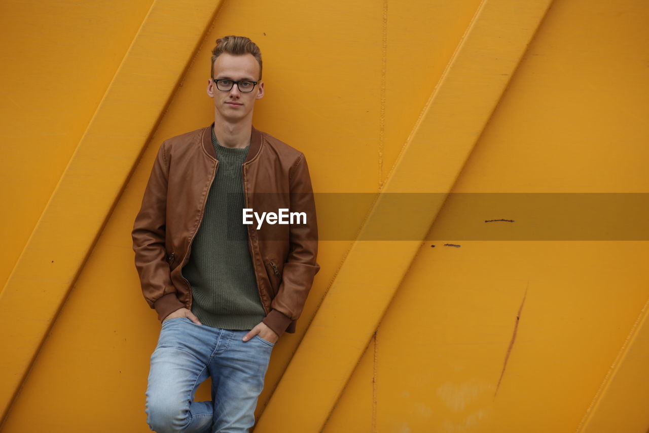 PORTRAIT OF YOUNG MAN STANDING ON YELLOW WALL