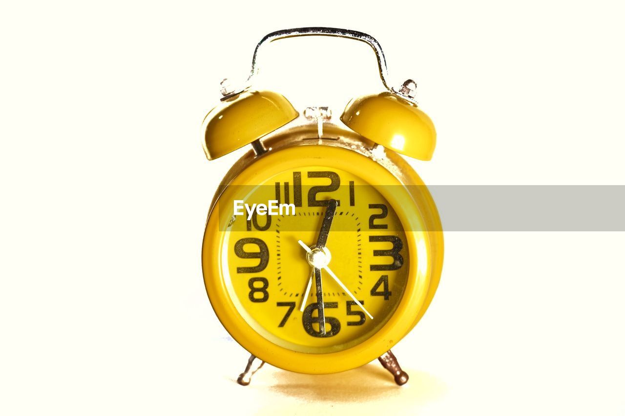 CLOSE-UP OF YELLOW CLOCK ON WHITE BACKGROUND