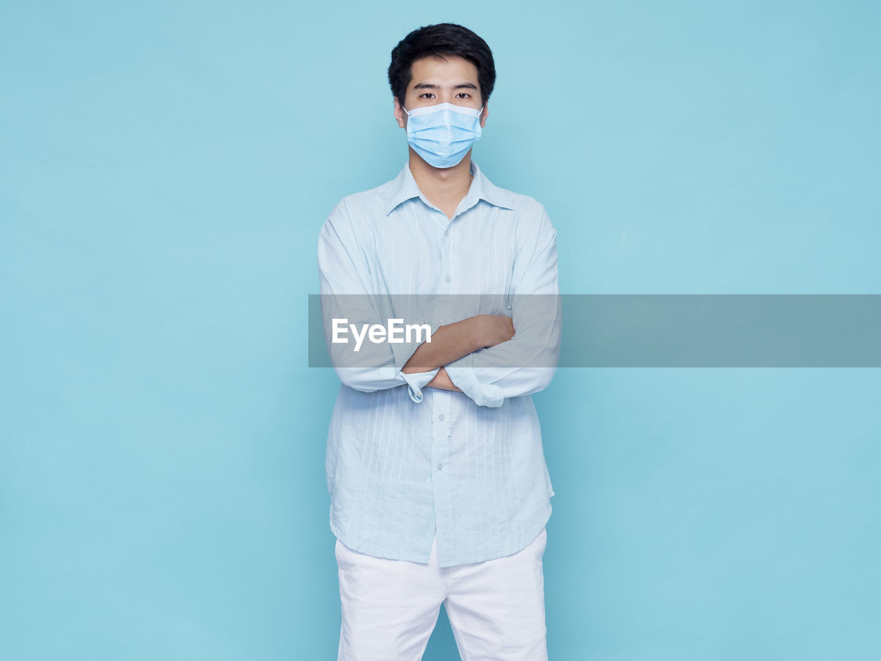 Portrait of young man wearing mask standing against blue background