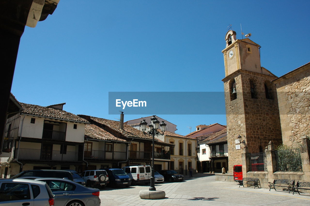 CARS ON STREET AMIDST BUILDINGS AGAINST CLEAR BLUE SKY