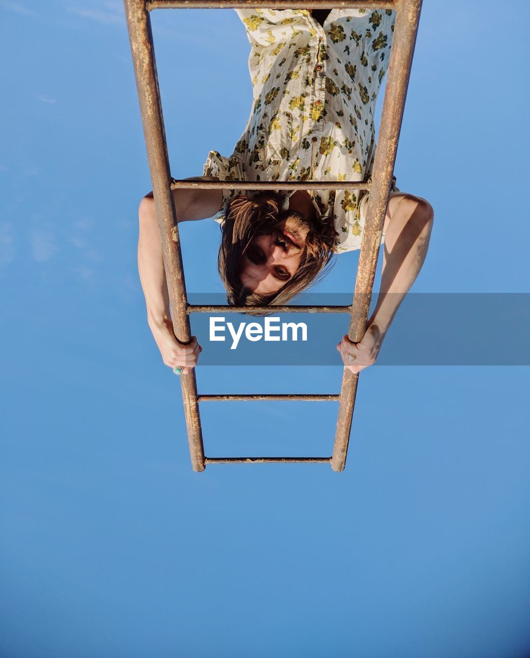 Low angle portrait of young man climbing on ladder against clear blue sky