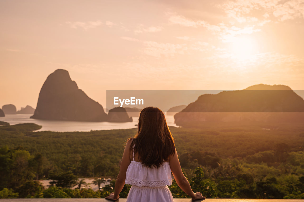REAR VIEW OF WOMAN LOOKING AT MOUNTAIN DURING SUNSET