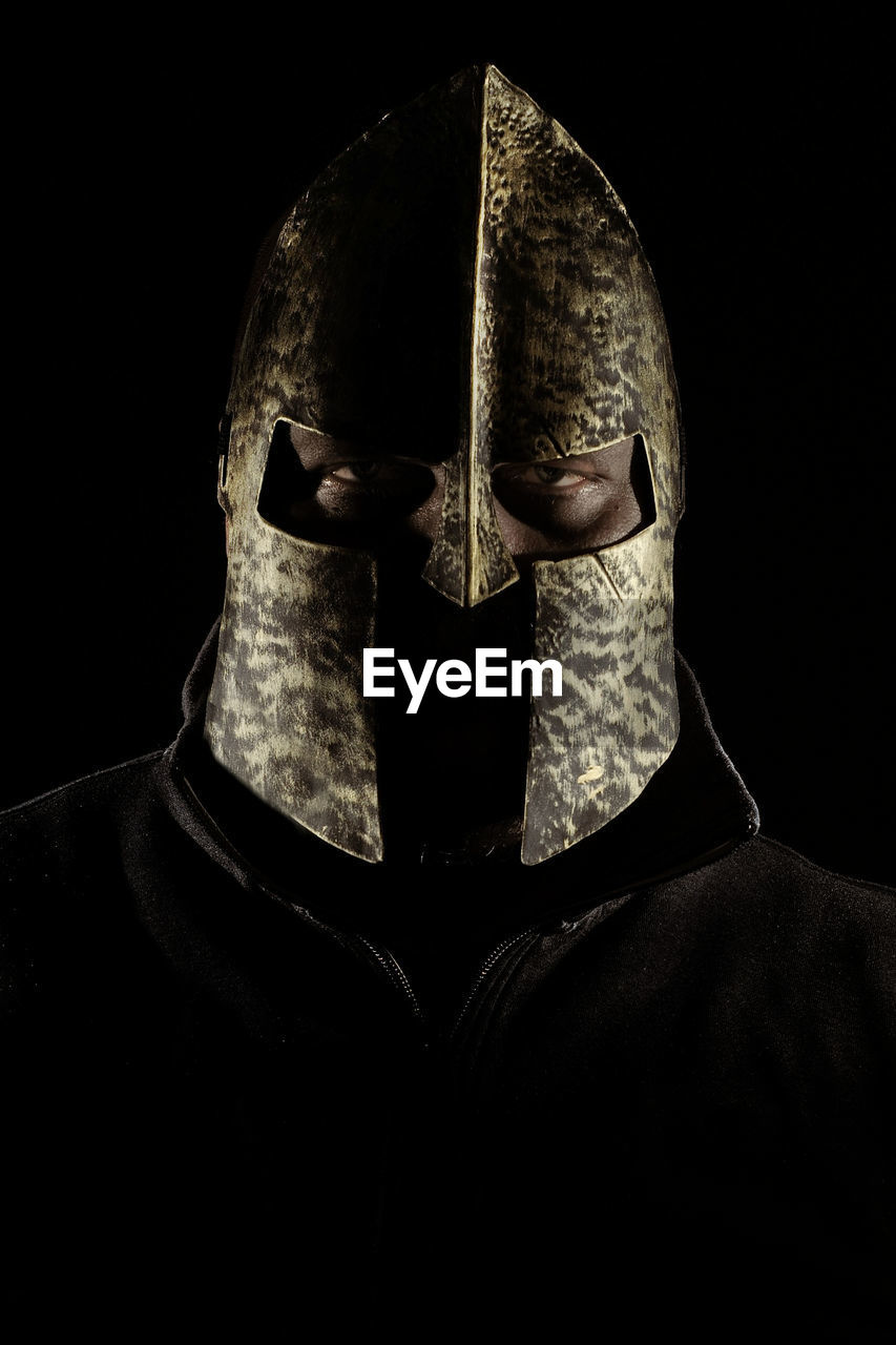 Close-up portrait of man wearing metal mask against black background