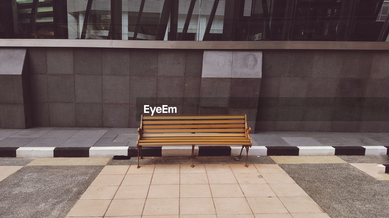 Empty bench by sidewalk against building in city