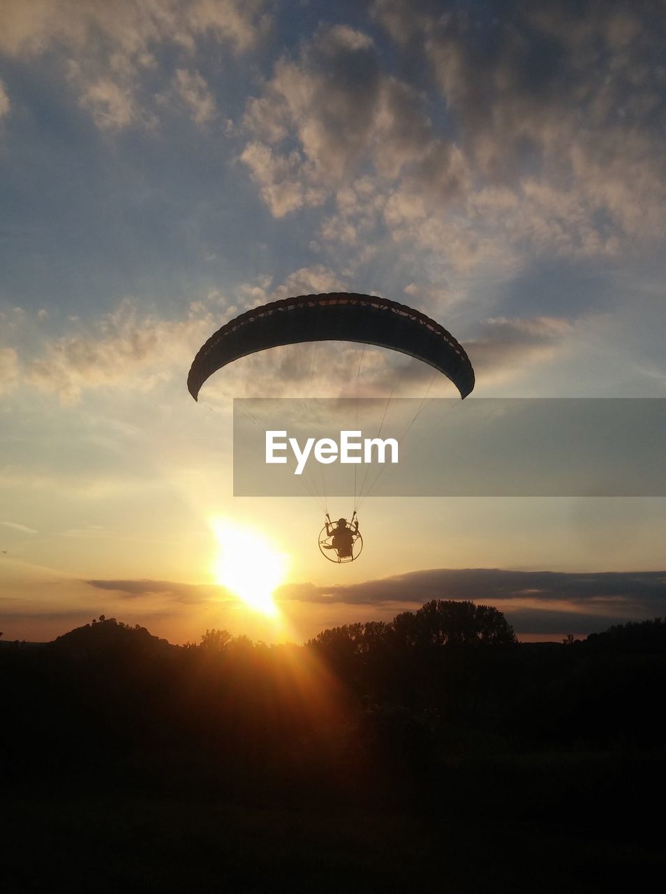 Silhouette person powered paragliding against sky during sunset