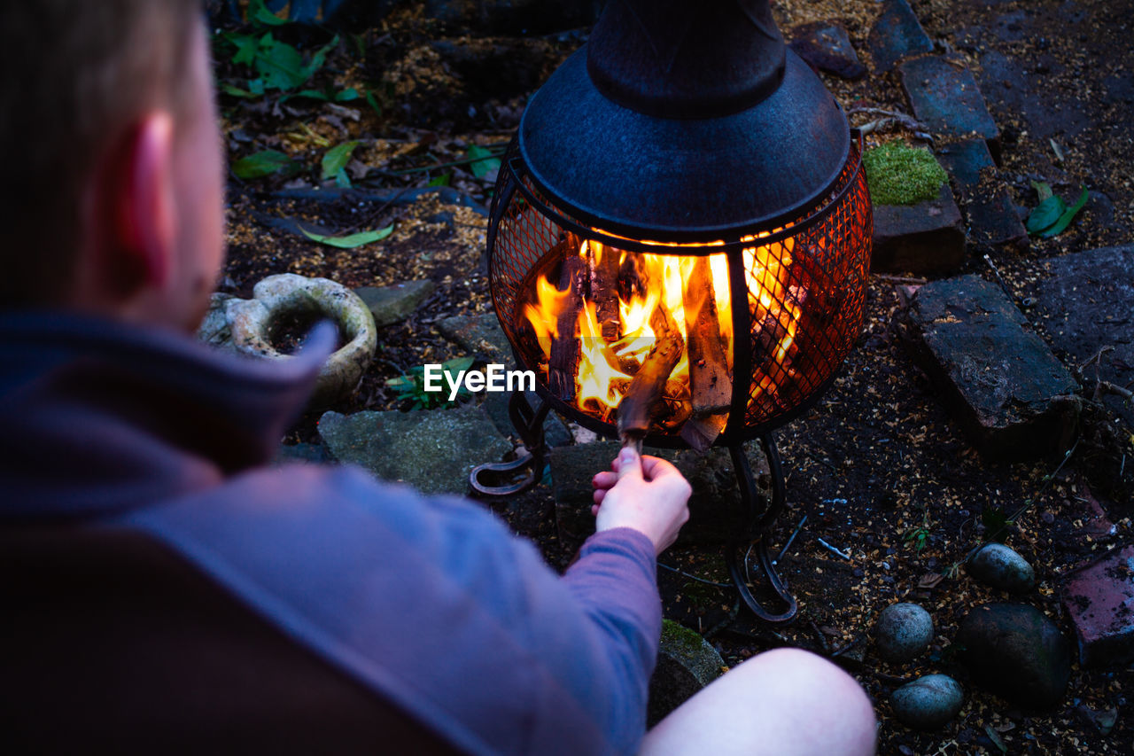 High angle view of young man warming hands over fire at night