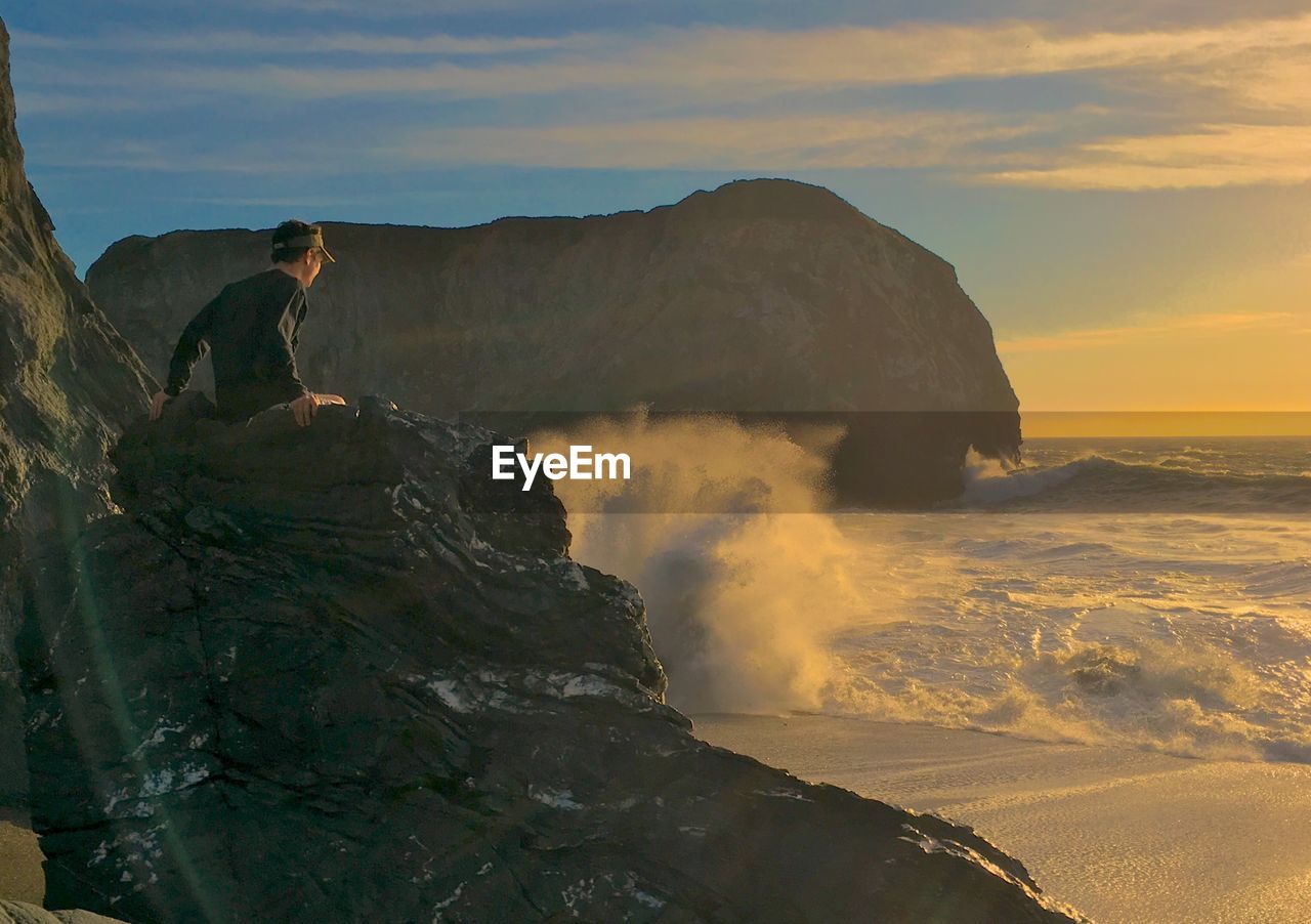 Man sitting on rock formation at beach during sunset