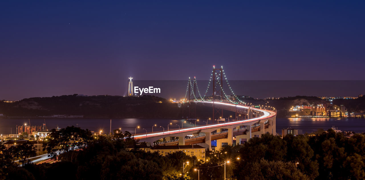 Illuminated 25 de abril bridge over tagus river by christ the king against sky at night