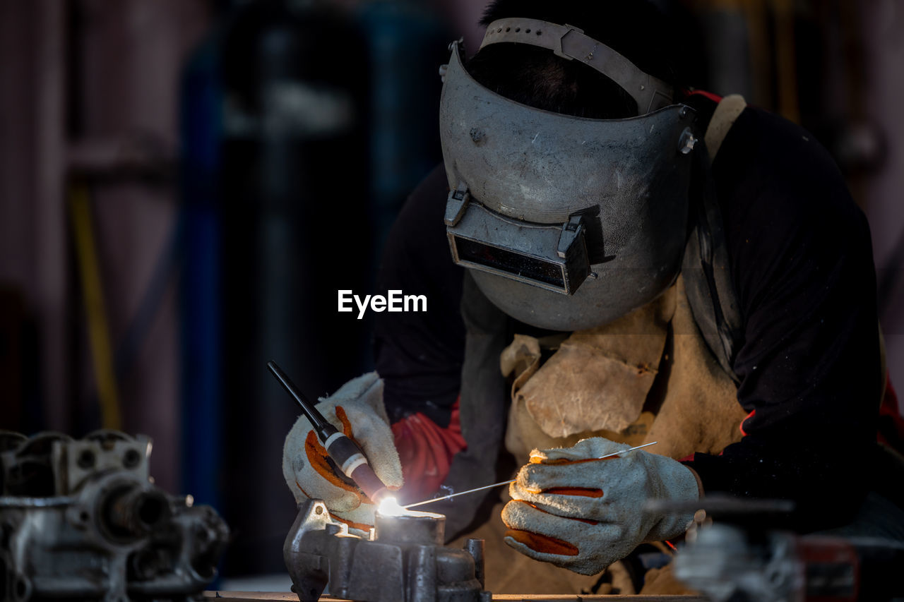 Welder in face mask welds with argon arc stainless steel welding, industrial worker at the factory.