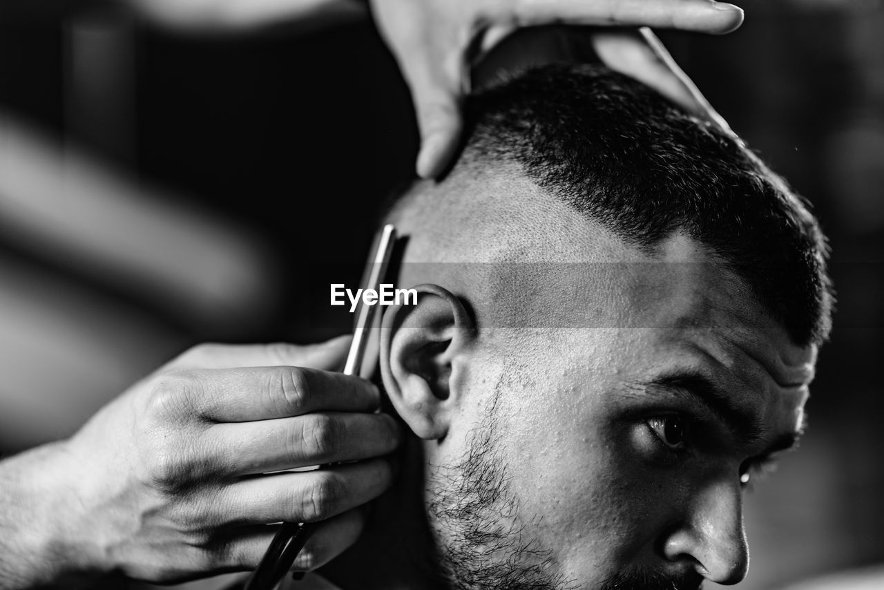 Cropped image of barber cutting man hair in shop