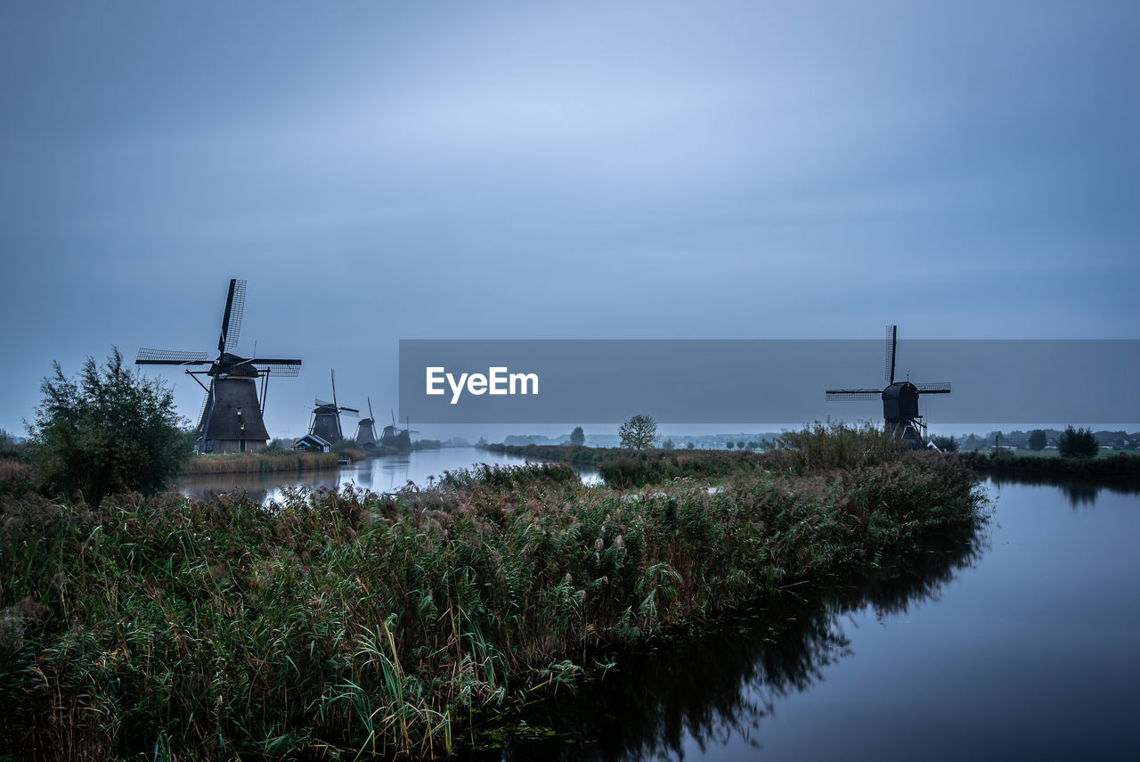 Traditional windmills by lake against sky