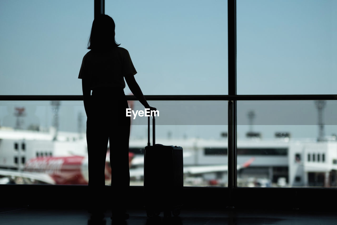 Rear view silhouette woman standing with luggage by window in airport