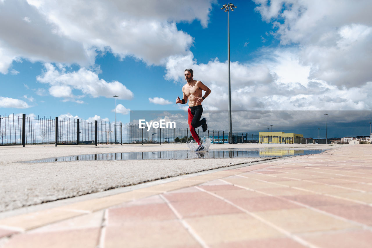 Mature man jogging on road against cloudy sky