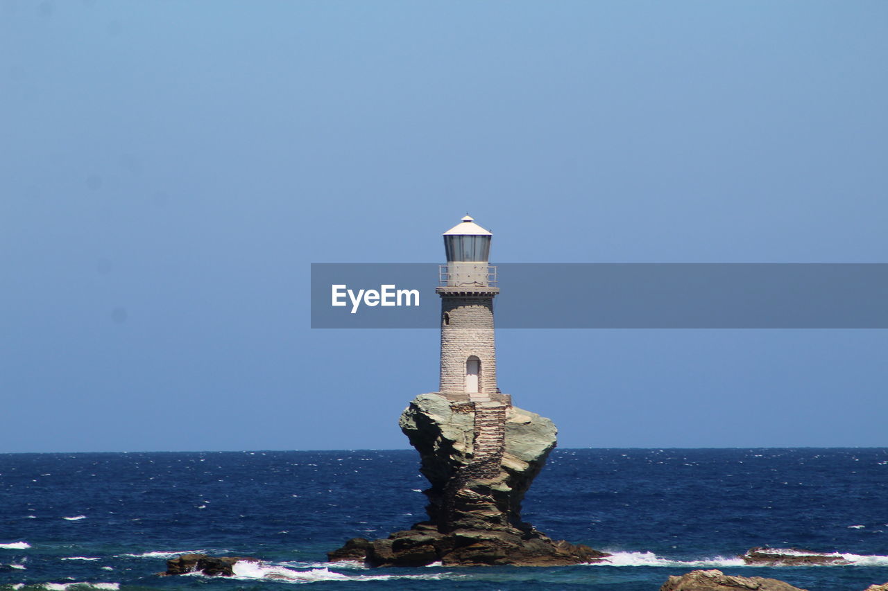 Lighthouse by sea against clear sky