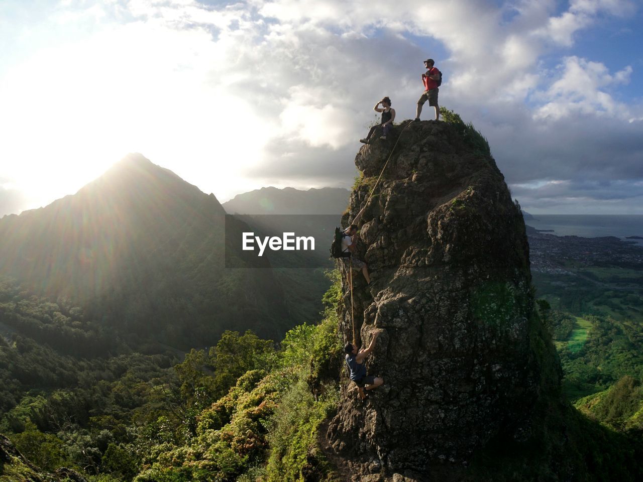 PEOPLE ON ROCK BY MOUNTAIN AGAINST SKY