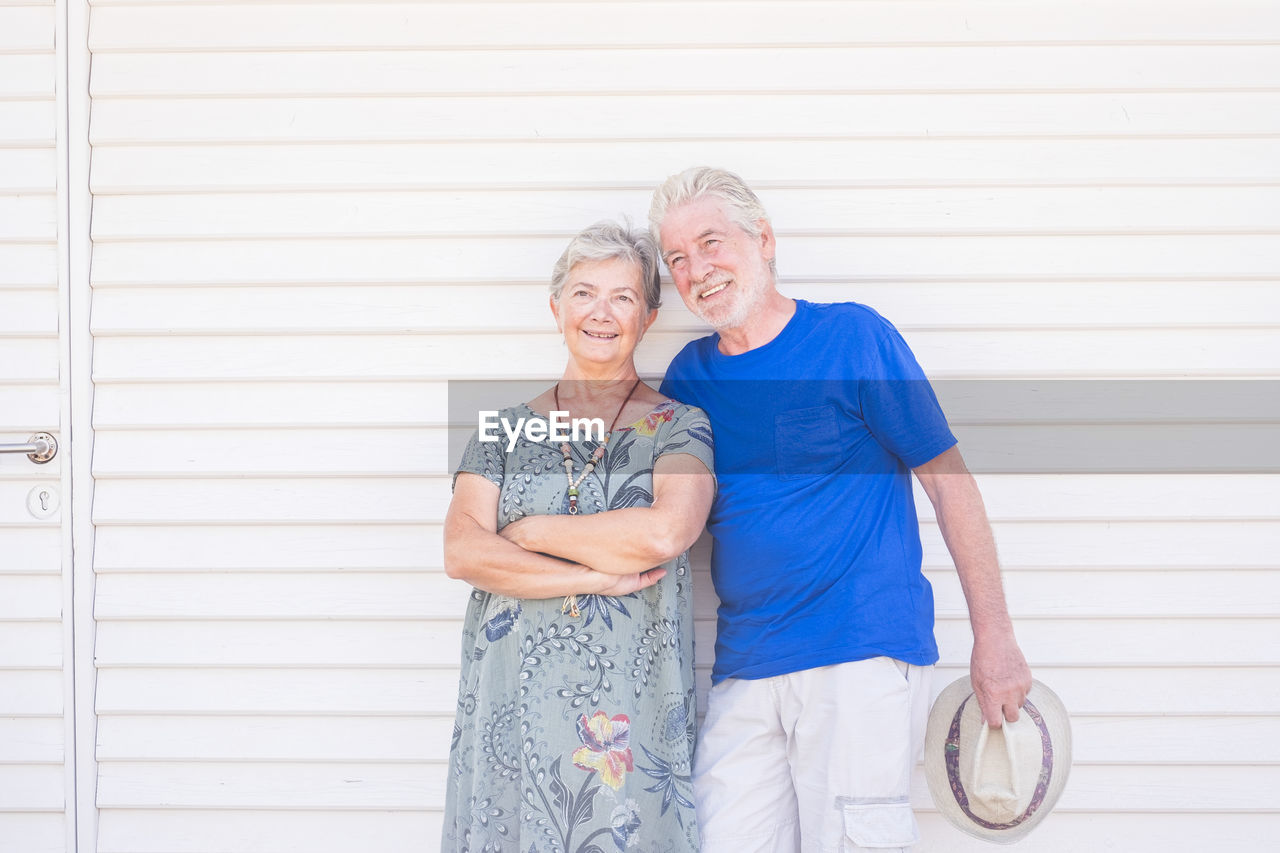 Smiling senior couple looking away while standing against wall