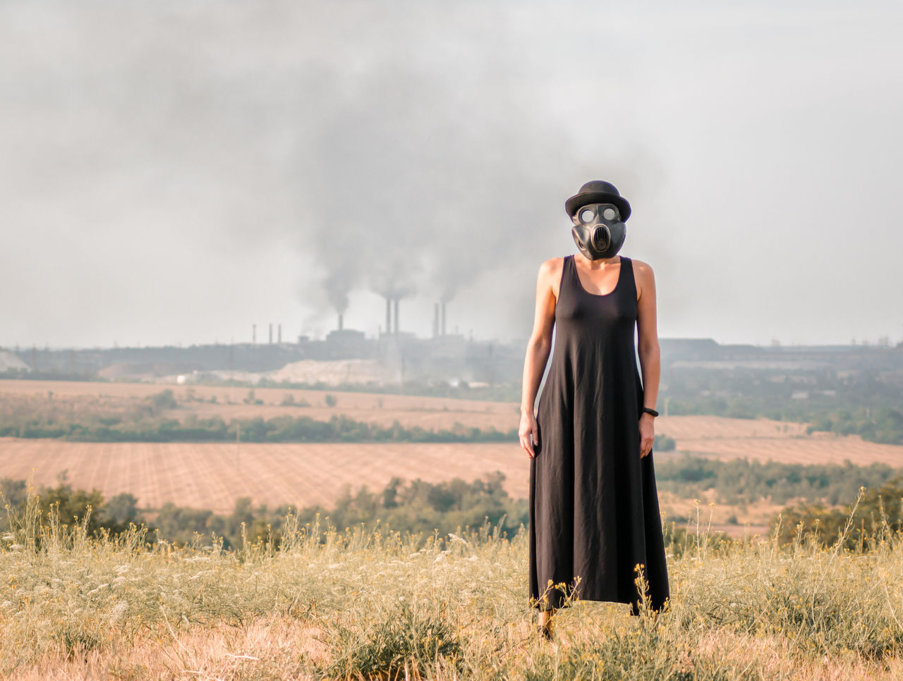 Woman wearing gas mask while standing on grass against sky