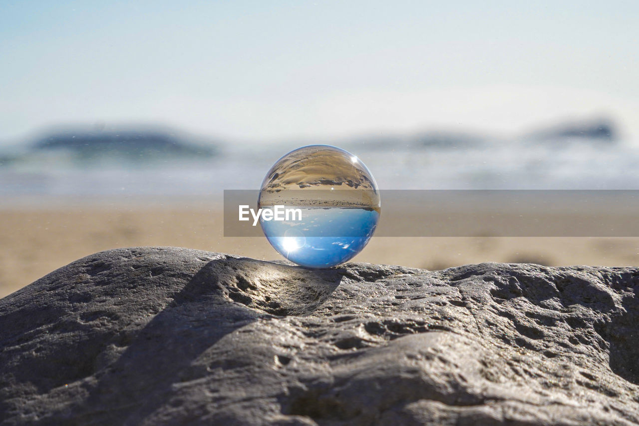 Photography crystal photo ball showing upside down reflection of sky beach and waves on rocks 