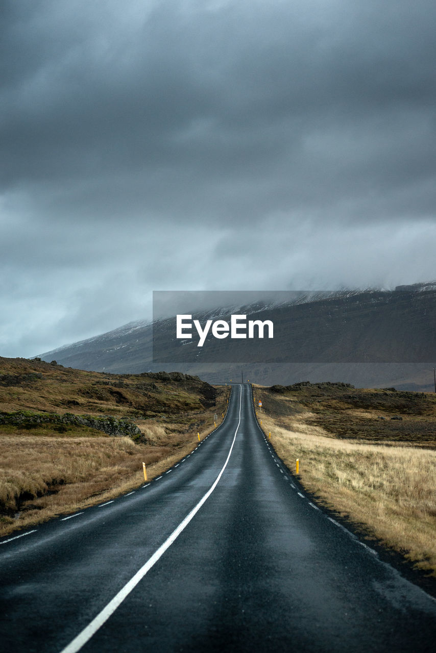 Empty road along landscape against cloudy sky