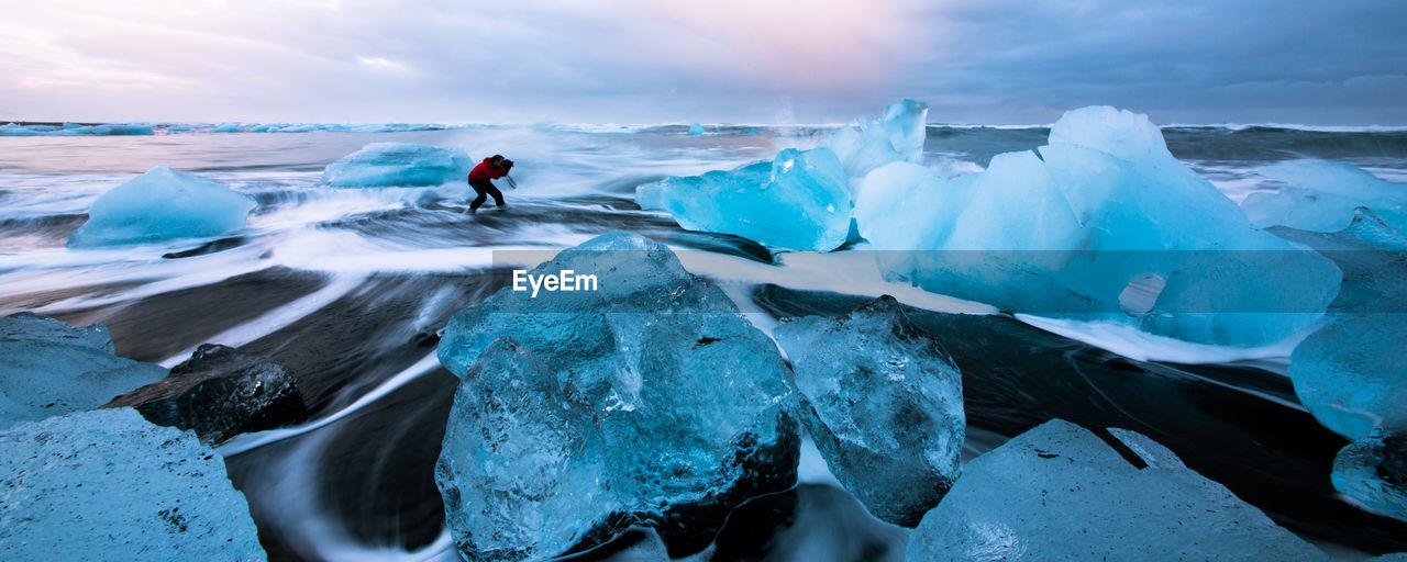 Panoramic view of woman standing at beach by icebergs during winter