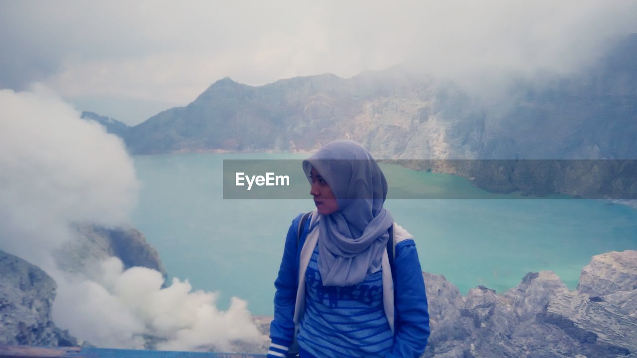 Woman wearing hijab sanding on mountain against lake