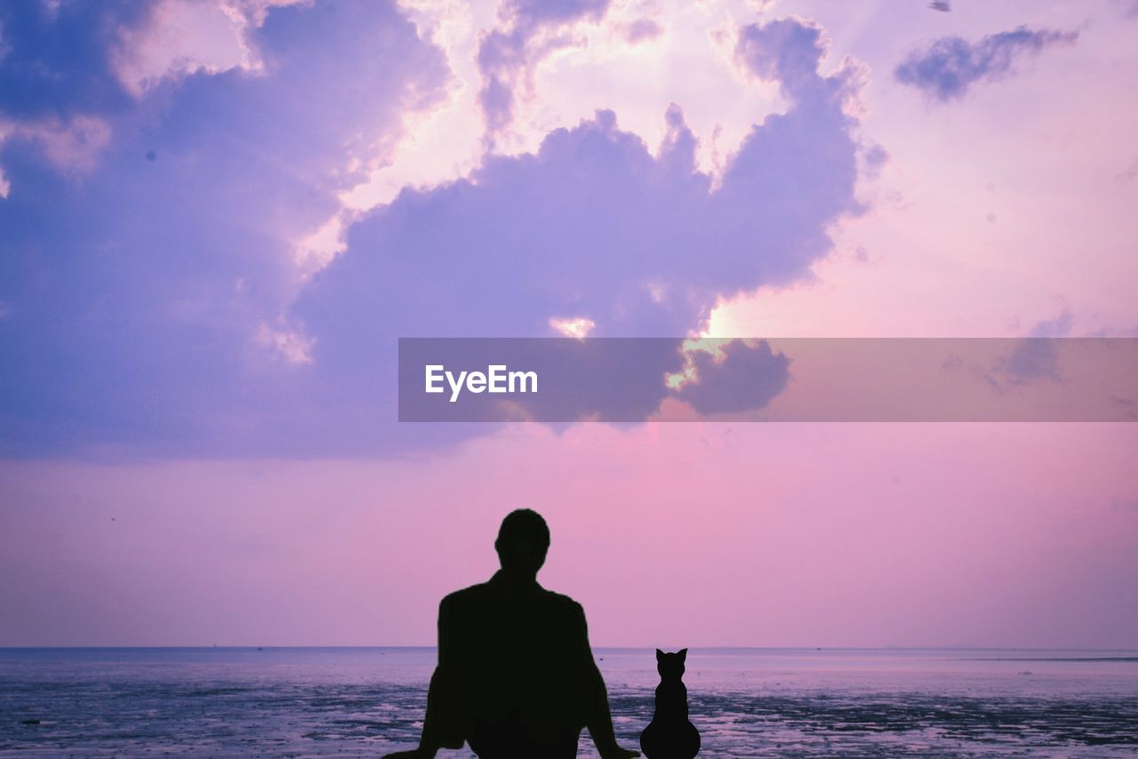 Rear view of silhouette man with cat looking at sea against dramatic sky during sunset