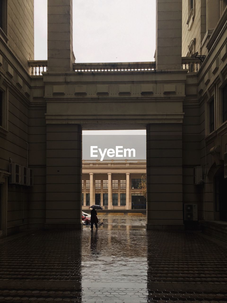 Man walking on wet street amidst buildings in city