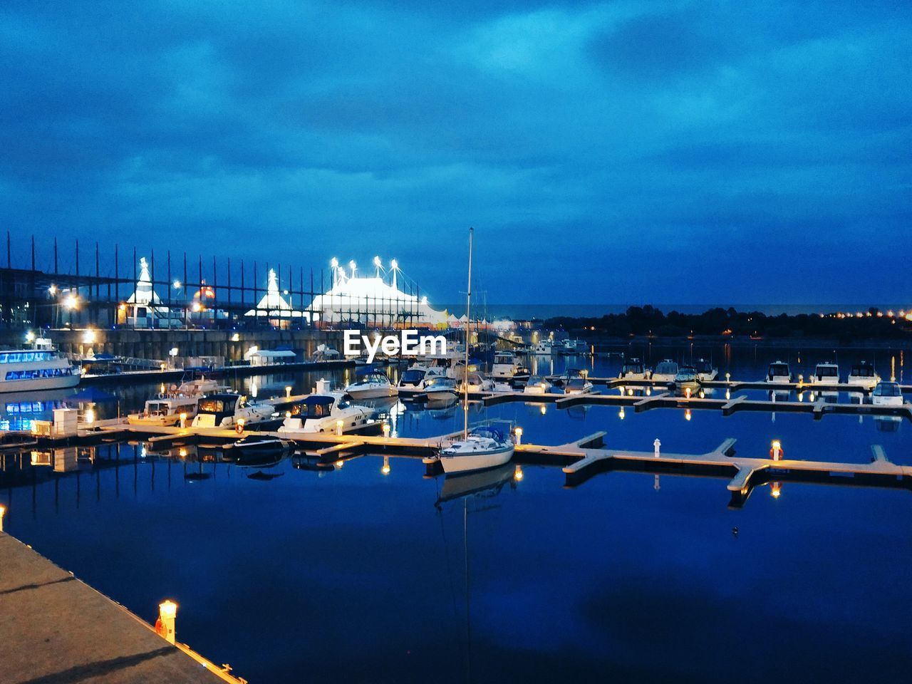 Sailboats moored on harbor against sky at night