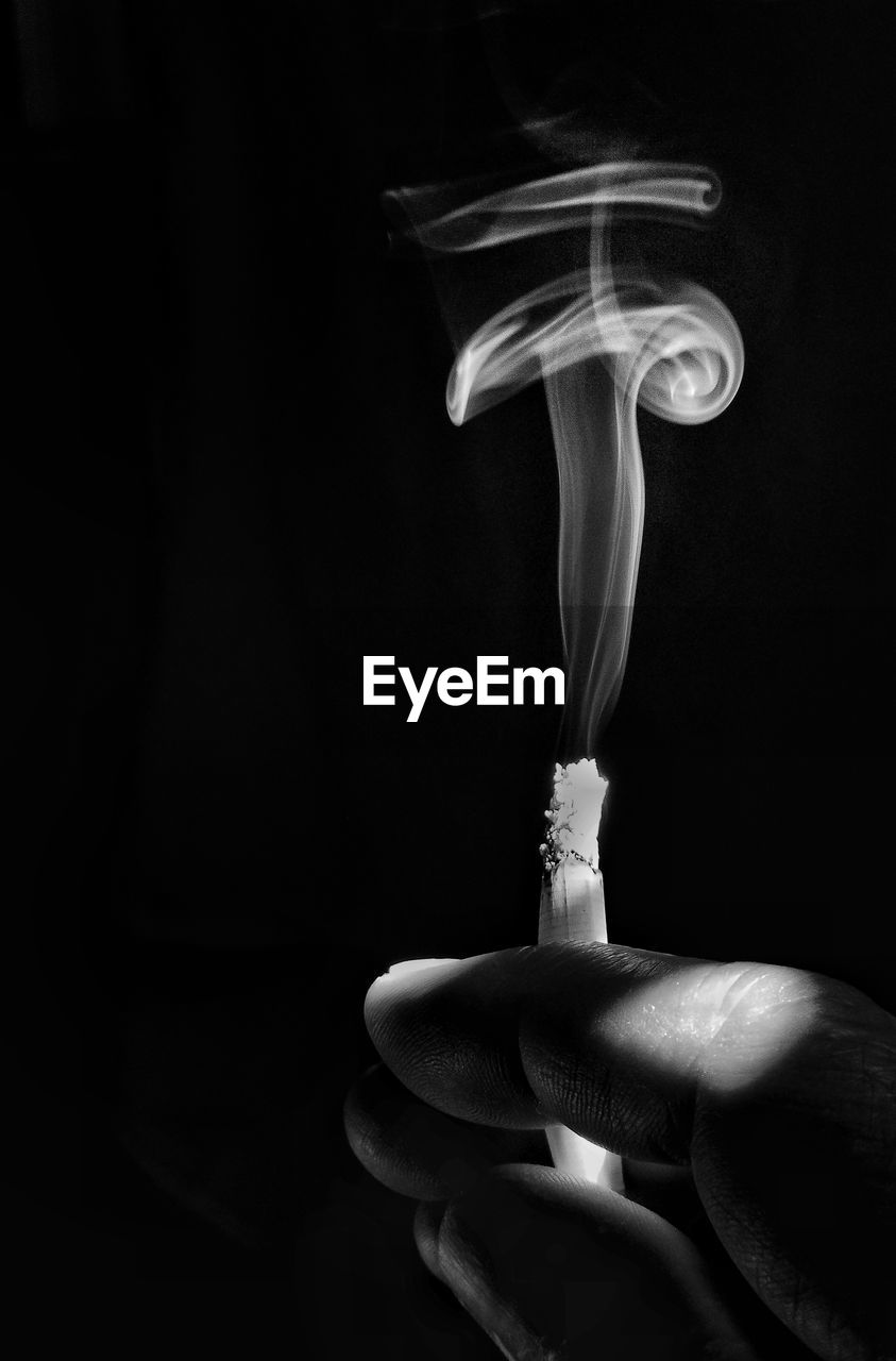 Close-up of hand holding cigarette against black background