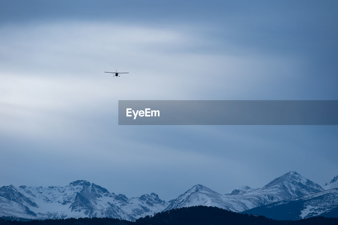 AIRPLANE FLYING OVER SNOWCAPPED MOUNTAIN AGAINST SKY