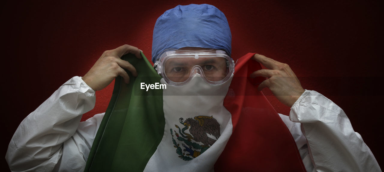 Portrait of man wearing flu mask and goggles against red background