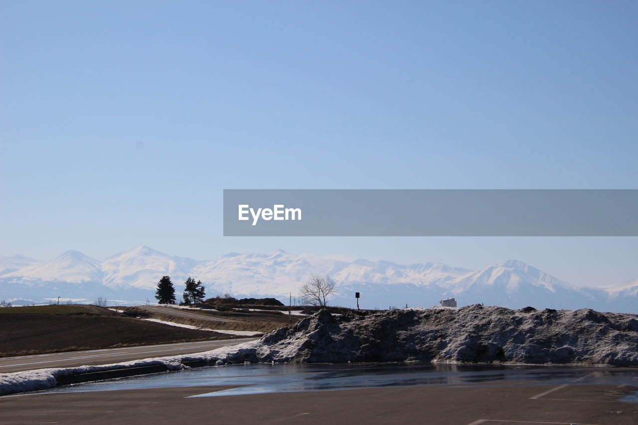 Road by snowcapped mountains against clear sky