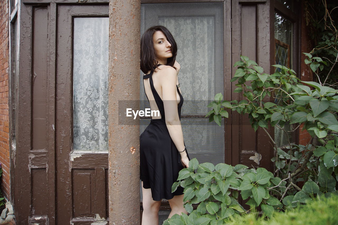 Portrait of beautiful woman standing against pole by house