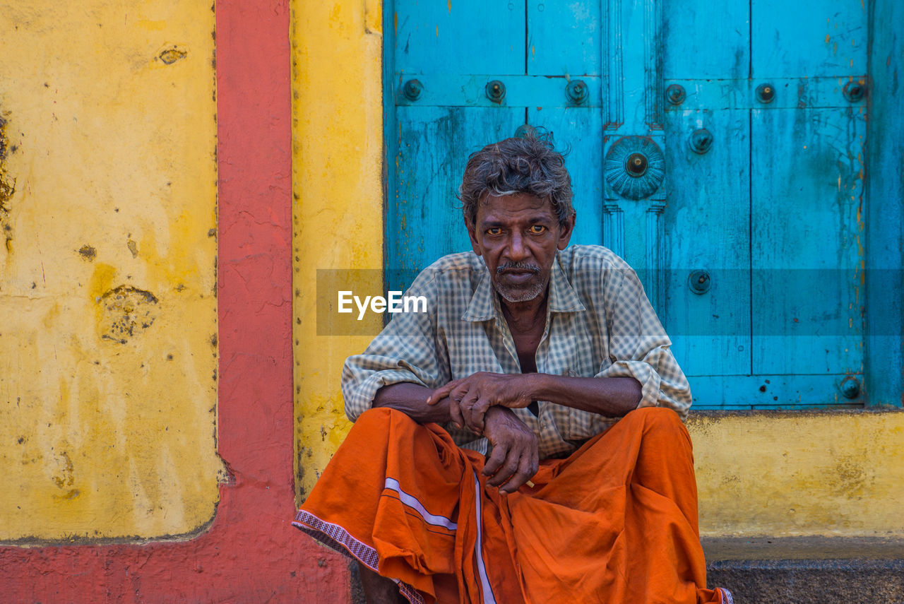 PORTRAIT OF MAN SITTING AGAINST BLUE DOOR