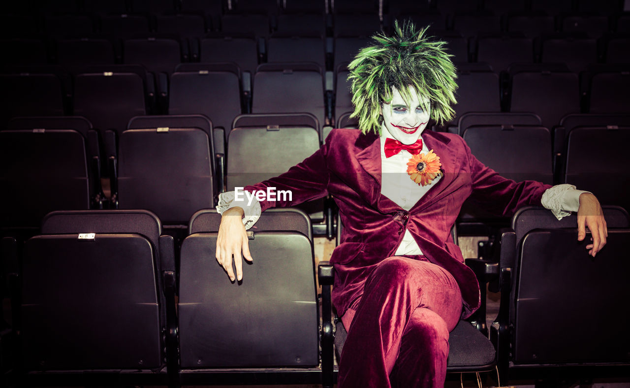 Portrait of man wearing clown costume sitting on chair