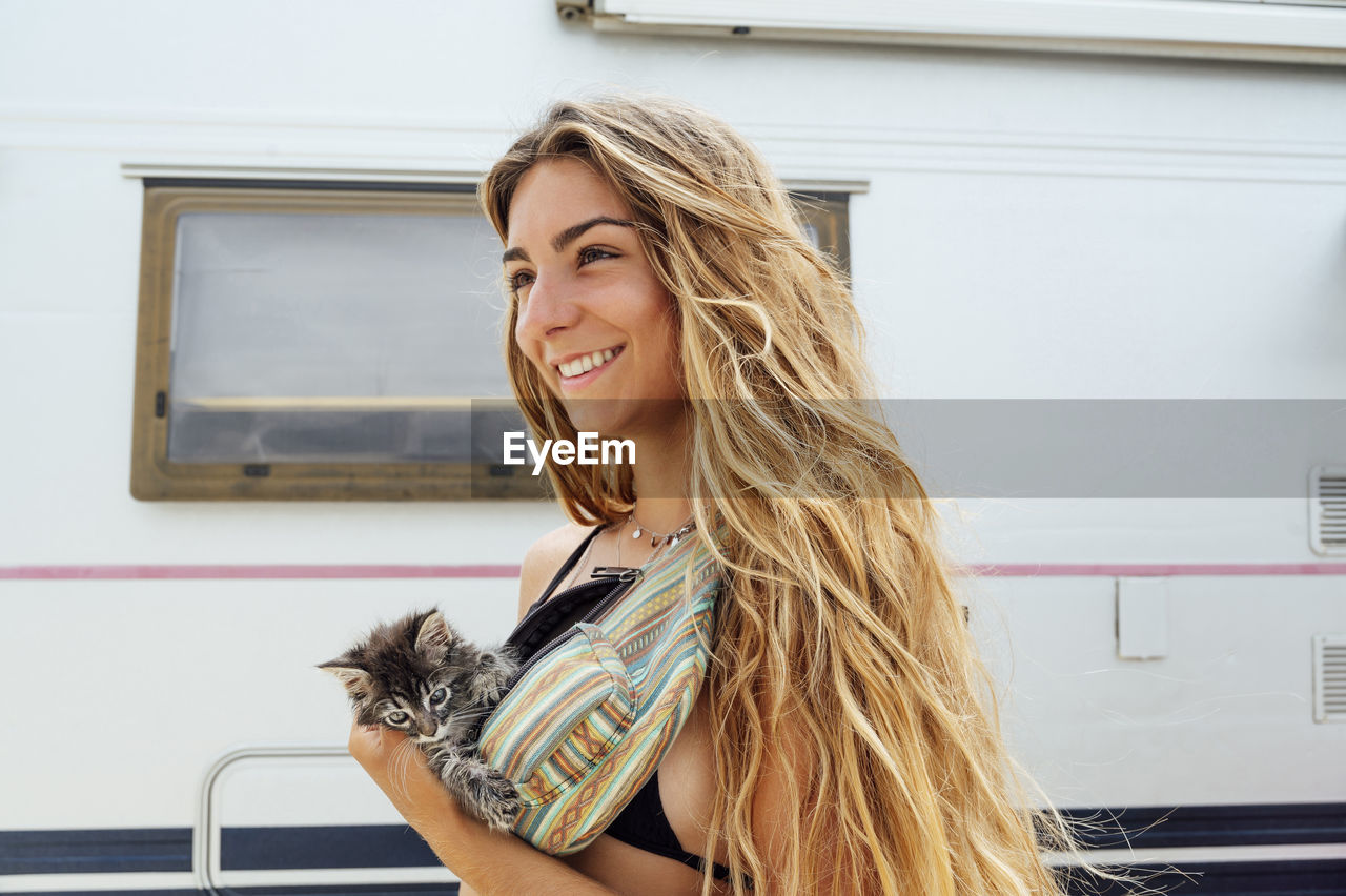 Smiling young woman with kitten in waist pack