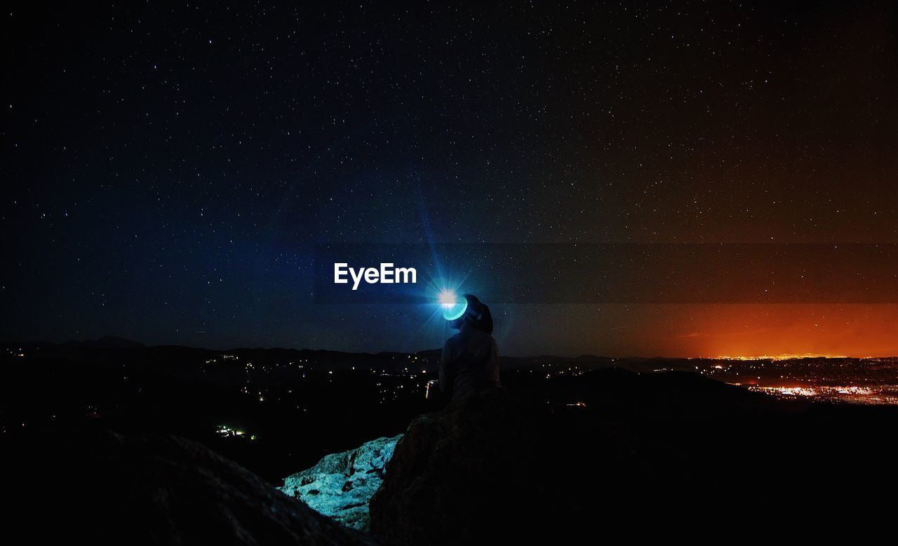 Silhouette woman with illuminated flashlight against star field