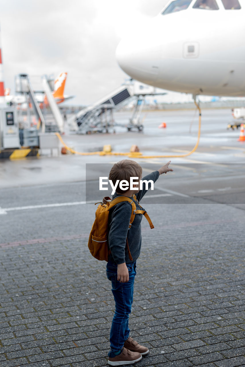 A little boy stands by the plane and points his finger at the pilot.