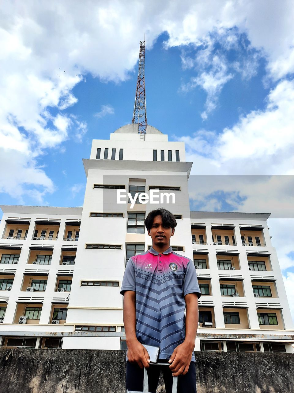 FULL LENGTH PORTRAIT OF YOUNG MAN STANDING AGAINST BUILDING