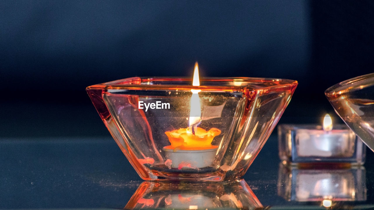 CLOSE-UP OF ILLUMINATED CANDLES ON GLASS