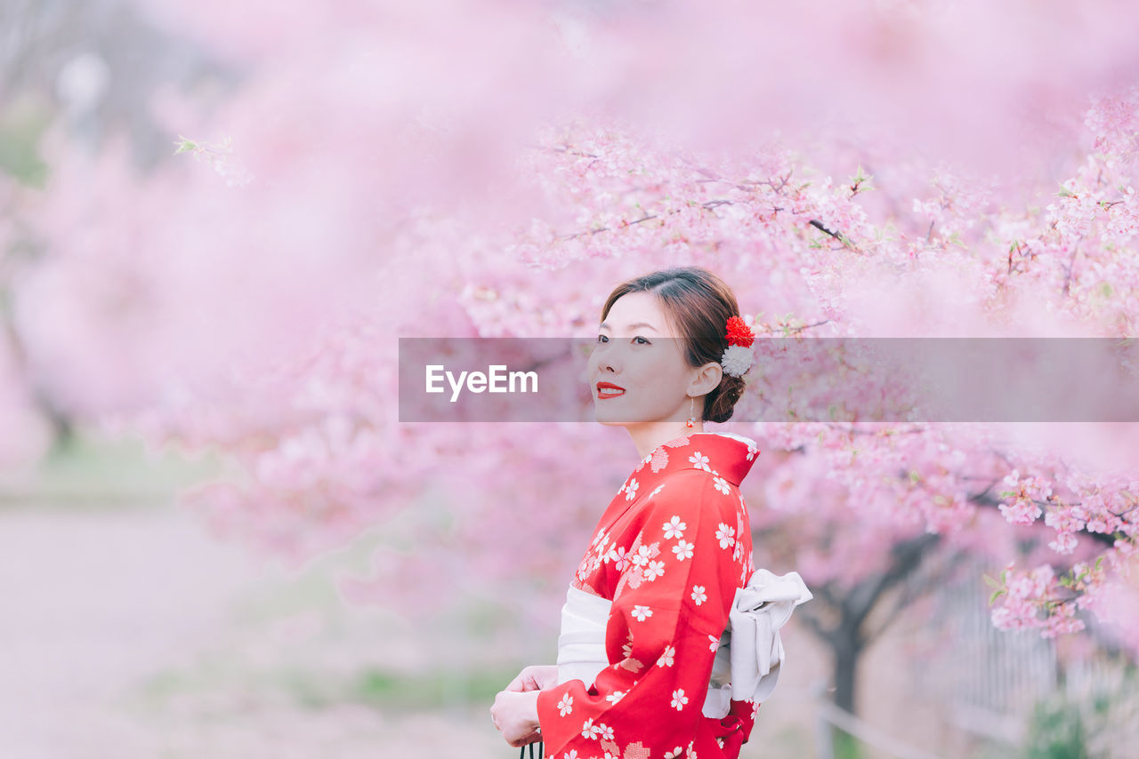 Side view of woman against pink cherry blossom trees