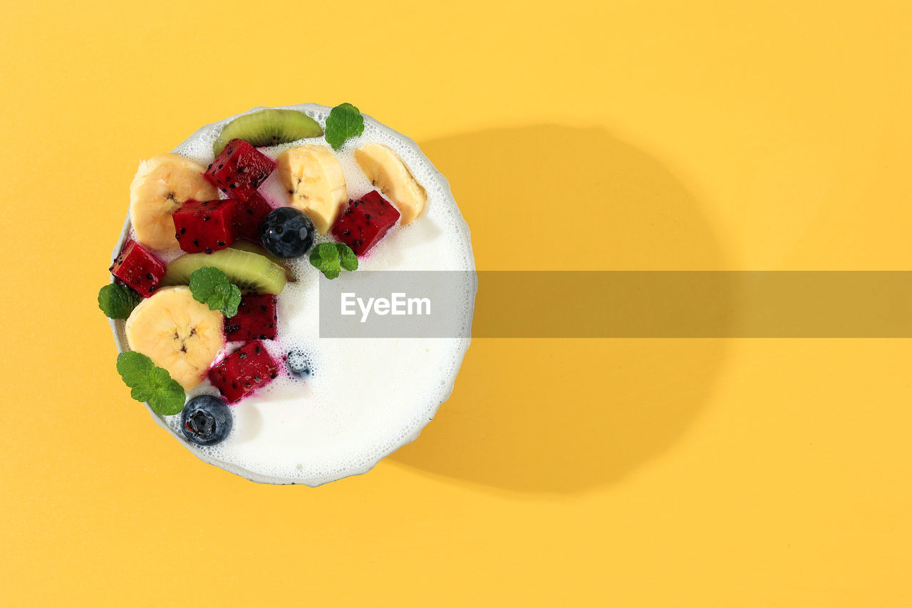 Yoghurt bowl with fresh fruit topping and mint leaves on yellow background. summer healthy concept 