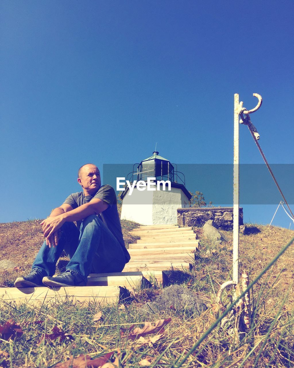 Man looking away while sitting on steps against clear sky